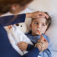 Mother checking temperature of her sick son who has thermometer in his mouth