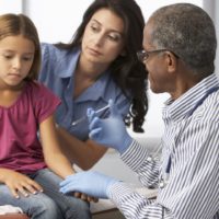 Doctor administering a vaccination to a young girl whilst being comforted by her mother