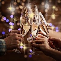 Clinking glasses of champagne in hands on bright lights background at Christmas