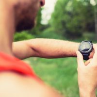 Man interval training on mountain forest trail checking looking at stopwatch smart watch